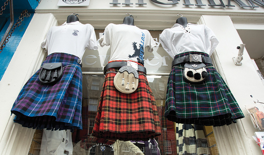 Three tartan kilts and sweaters hung outside a shop
