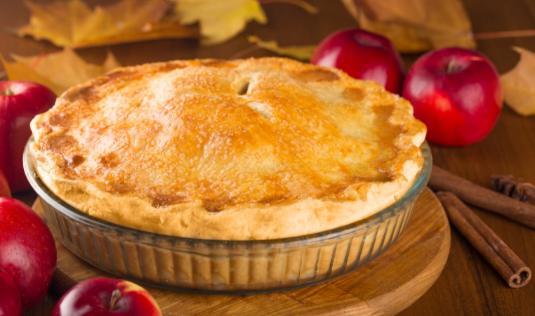 An Irish-style apple pie, on a wooden platter surrounded by apples